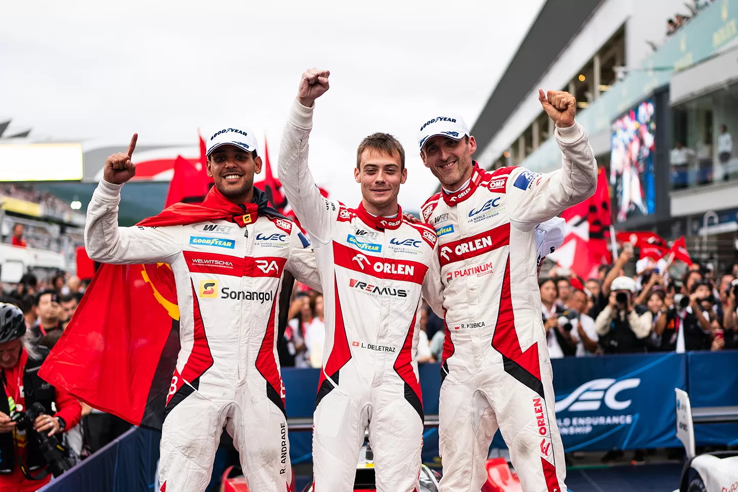 Three drivers cheering together dressed in white and red