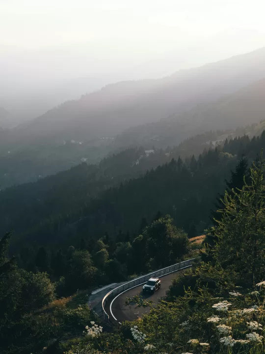 Car driving round mountain bend with open vista behind it