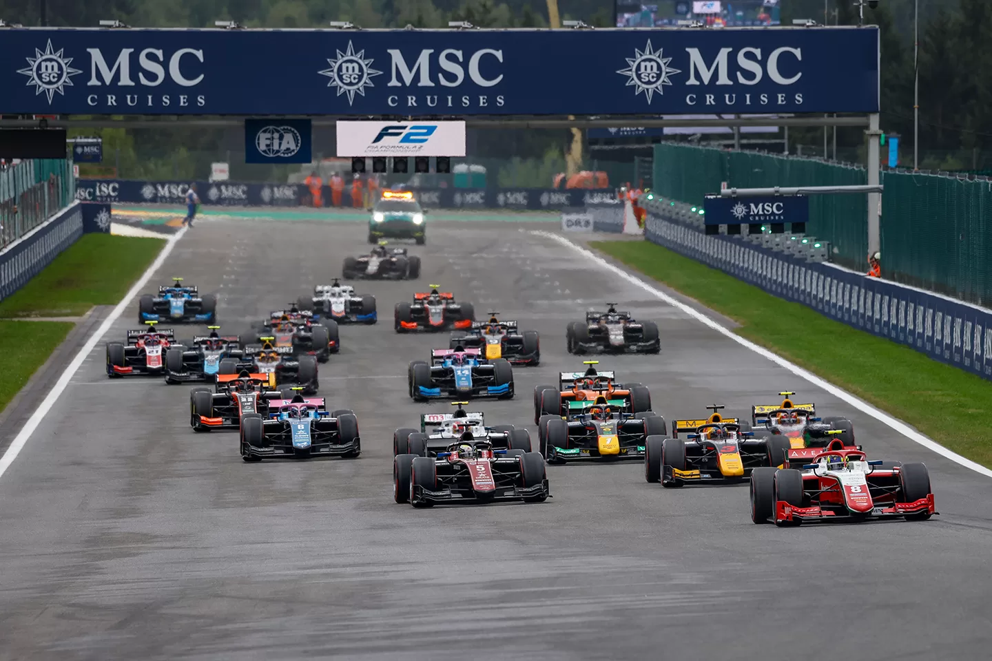 Racing cars all passing under a banner on a track