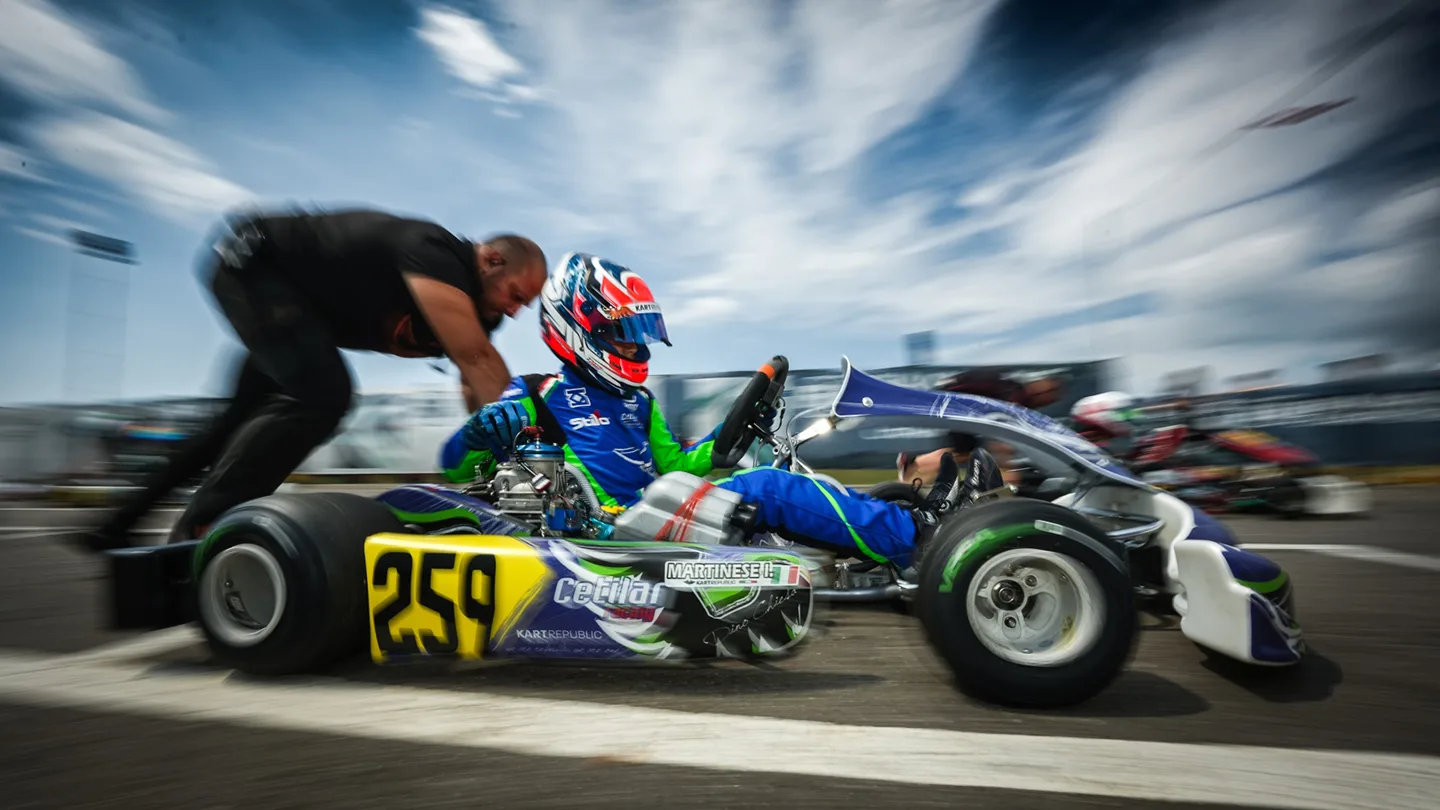 Man pushing kart with karting driver on tarmac