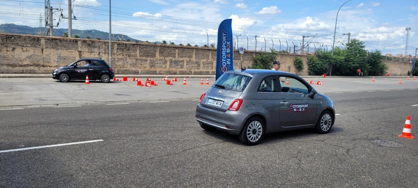 Two small cars go around a set of bright orange cones