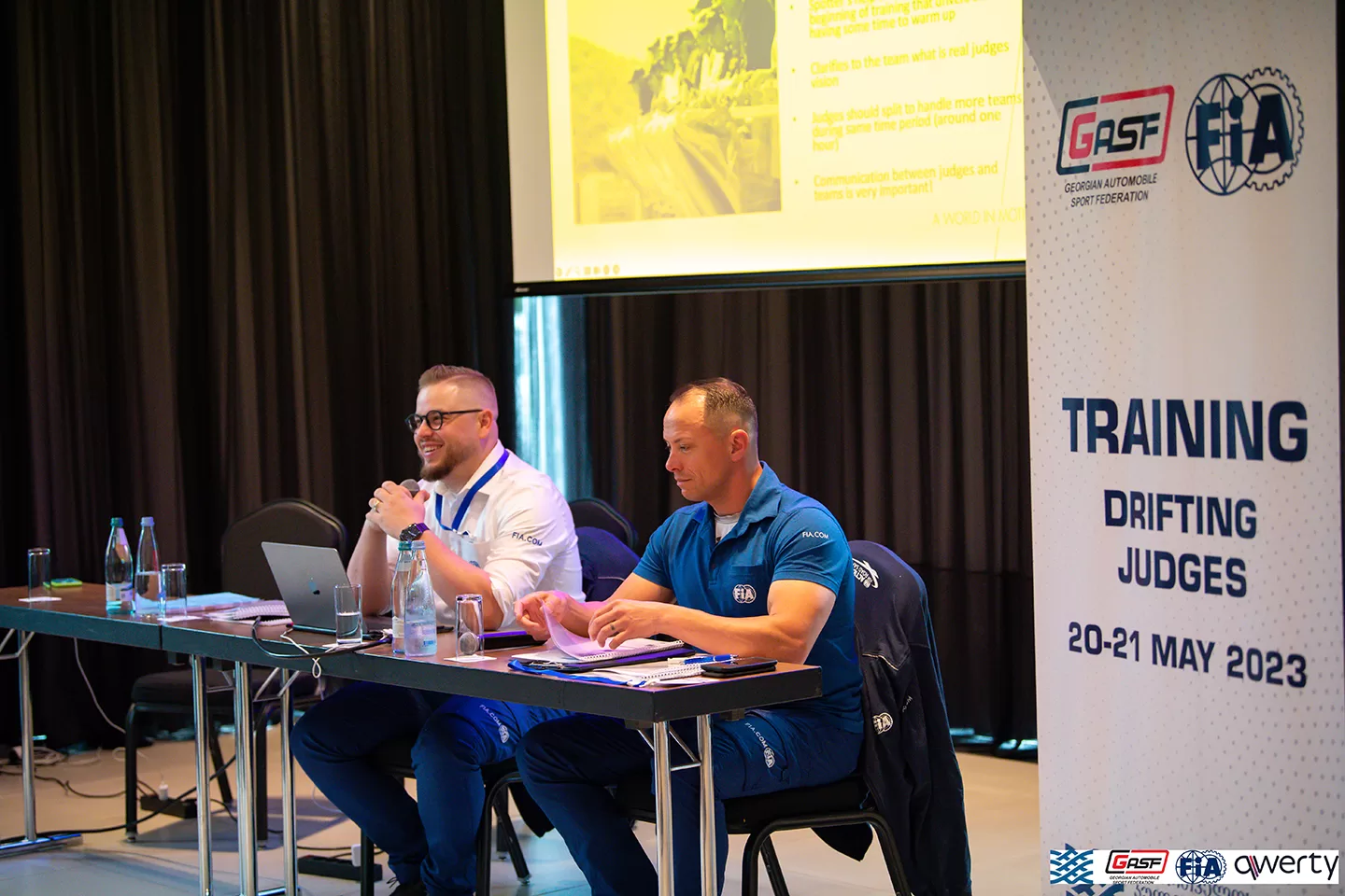 Two men speaking and smiling whilst surrounded by banners with 'training' written on them