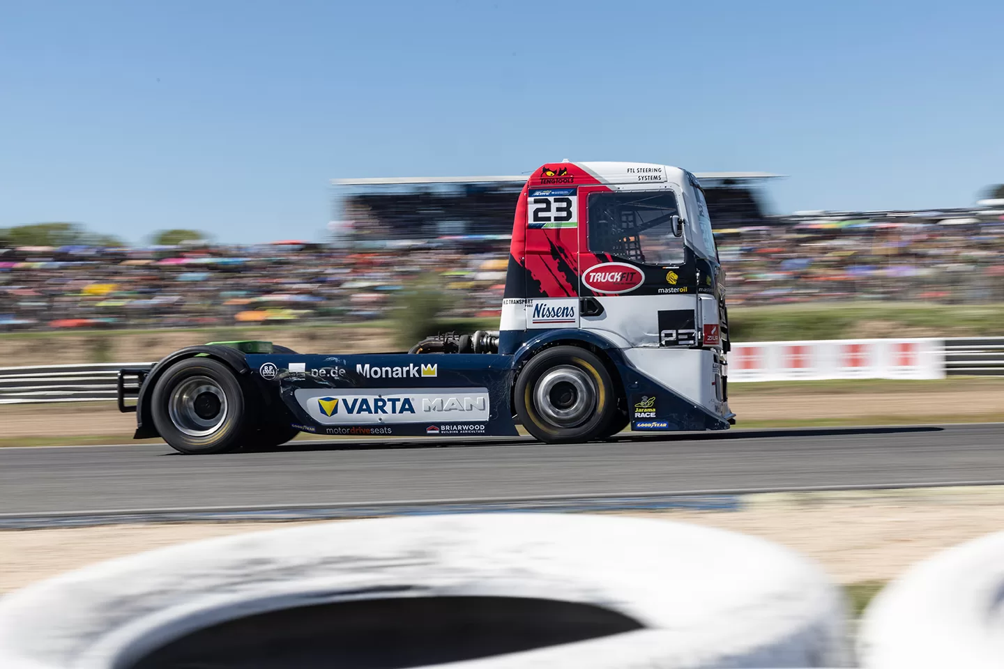 White, blue and red truck racing and photographed from the side