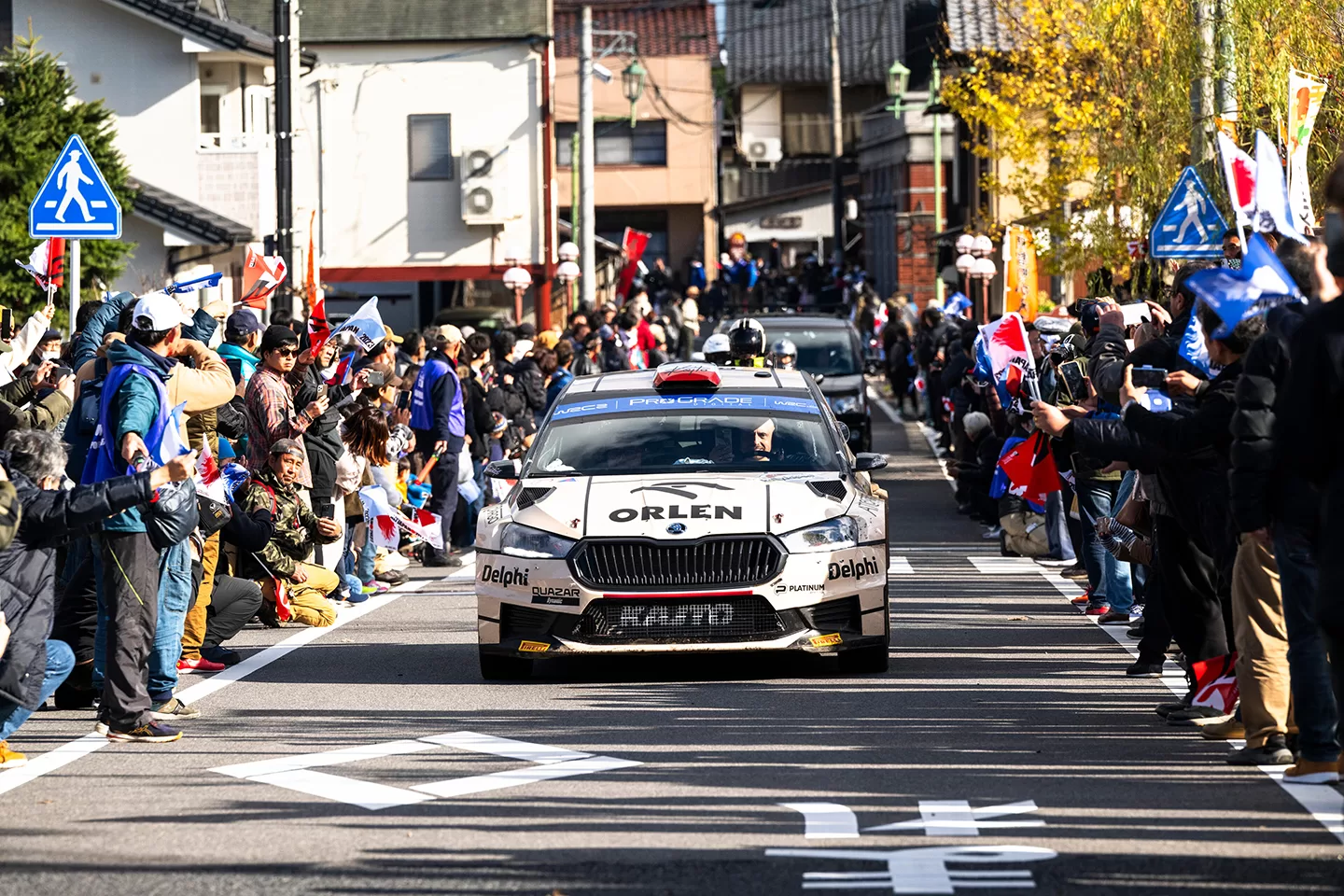 White car on a road with cheering crowds