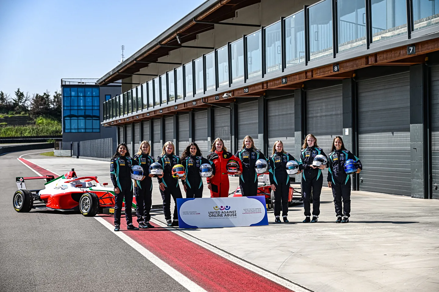 Group of young girls wearing racing tracksuits, with one in the middle wearing a red tracksuit