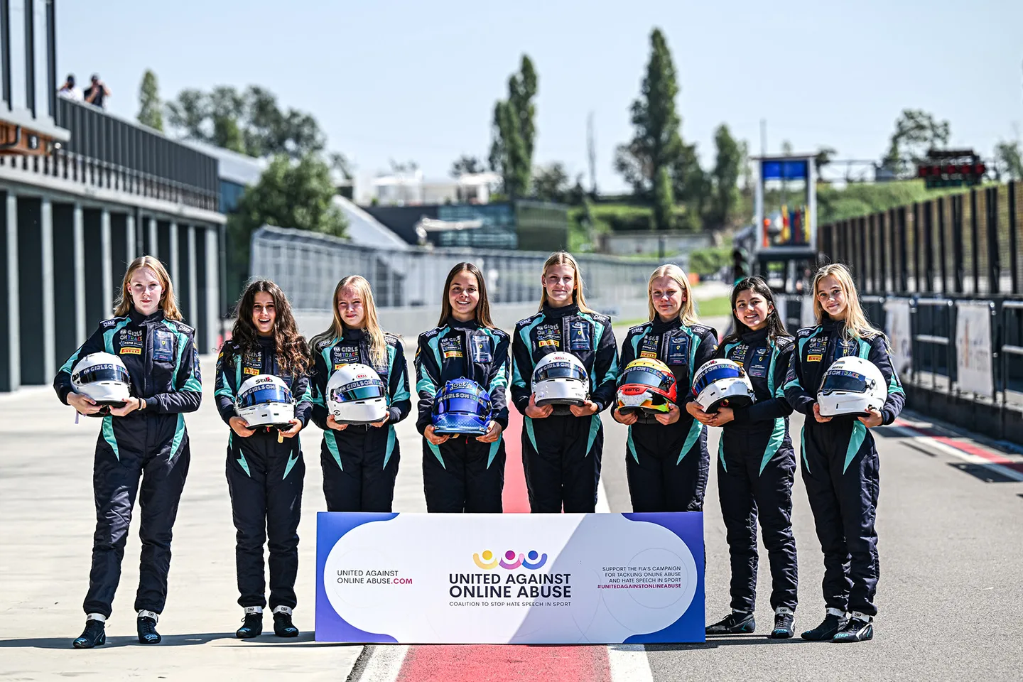 Group of young girls wearing racing jumpsuits and holding helmets in front of them 