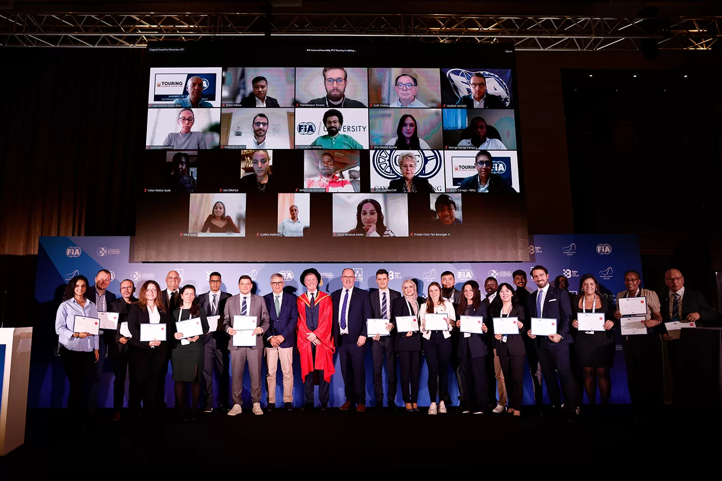 Group of graduates holding their certificates with a number of people joined remotely on a screen above them