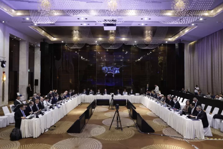 A conference room with tables arranged in a U shape with attendees sat around them