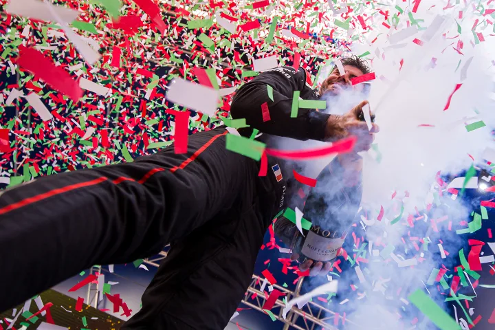 Racing driver with helmet on walking through confetti and smoke