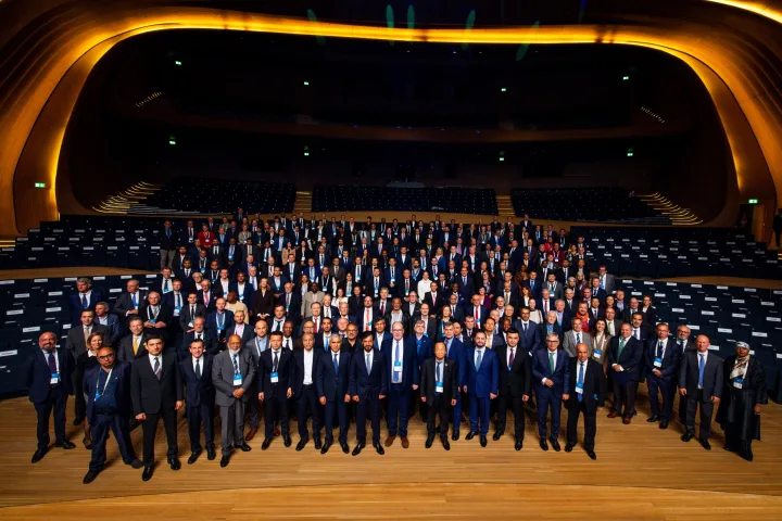 Large group of people gathered together in a large hall. All are wearing smart business wear.